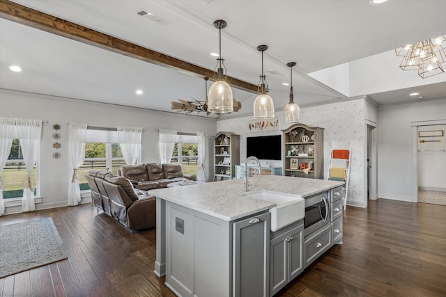 kitchen with dark hardwood / wood-style flooring, stainless steel microwave, sink, a kitchen island with sink, and decorative light fixtures