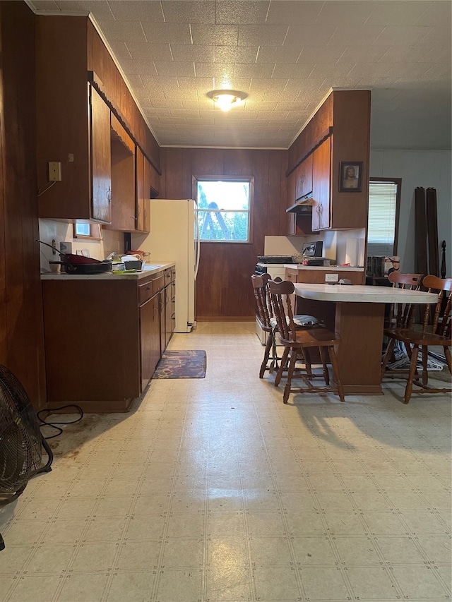 kitchen featuring wooden walls, white refrigerator, stainless steel range oven, and a breakfast bar area