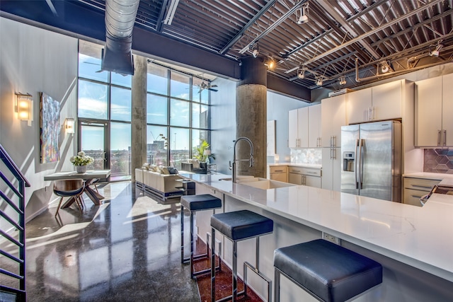 kitchen with tasteful backsplash, a high ceiling, concrete flooring, sink, and stainless steel fridge with ice dispenser