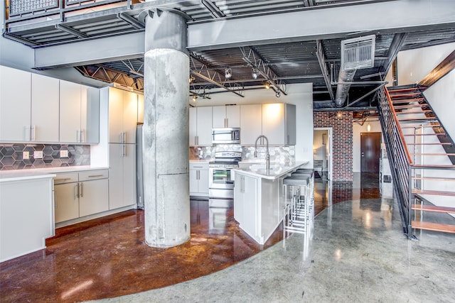 kitchen featuring appliances with stainless steel finishes, a breakfast bar, white cabinets, a center island with sink, and sink