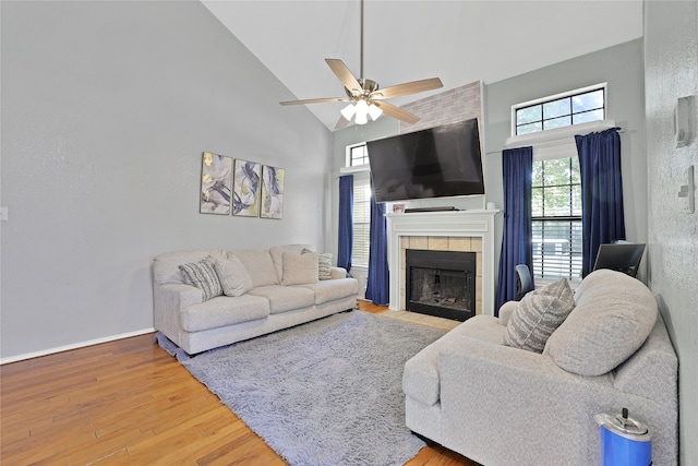 living room with ceiling fan, hardwood / wood-style flooring, a tiled fireplace, and high vaulted ceiling