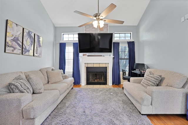 living room featuring a tiled fireplace, ceiling fan, vaulted ceiling, and light hardwood / wood-style floors