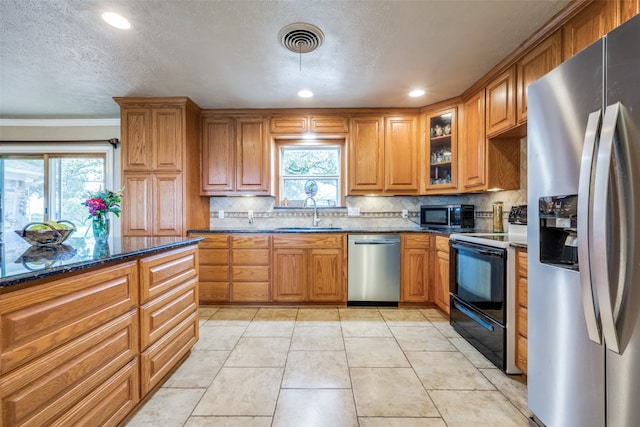 kitchen featuring dark stone counters, stainless steel appliances, a healthy amount of sunlight, and tasteful backsplash