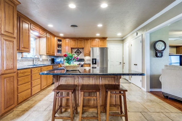 kitchen with a kitchen island, stainless steel appliances, dark stone countertops, a breakfast bar area, and crown molding