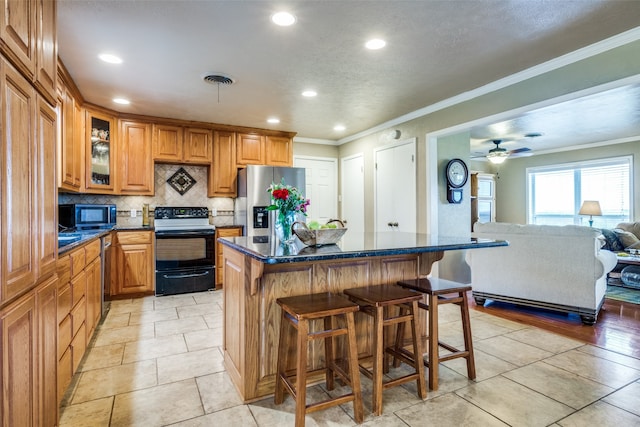 kitchen featuring appliances with stainless steel finishes, a breakfast bar, crown molding, a center island, and ceiling fan