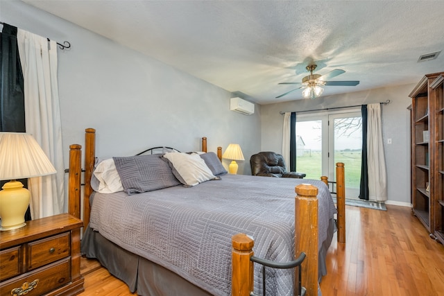 bedroom with ceiling fan, a wall mounted air conditioner, light wood-type flooring, and access to exterior