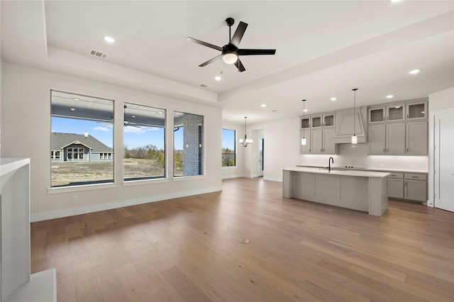 kitchen featuring gray cabinets, ceiling fan with notable chandelier, decorative light fixtures, tasteful backsplash, and a kitchen island with sink