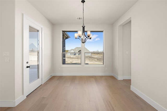 unfurnished dining area with light wood-type flooring, visible vents, baseboards, and an inviting chandelier