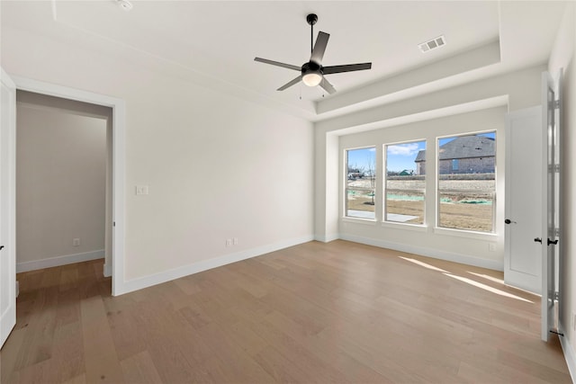 empty room featuring baseboards, visible vents, a ceiling fan, a tray ceiling, and light wood-style floors