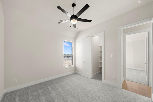 unfurnished bedroom featuring a walk in closet, light colored carpet, lofted ceiling, and ceiling fan