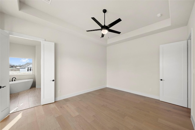 unfurnished bedroom with light wood finished floors, a raised ceiling, a ceiling fan, and baseboards