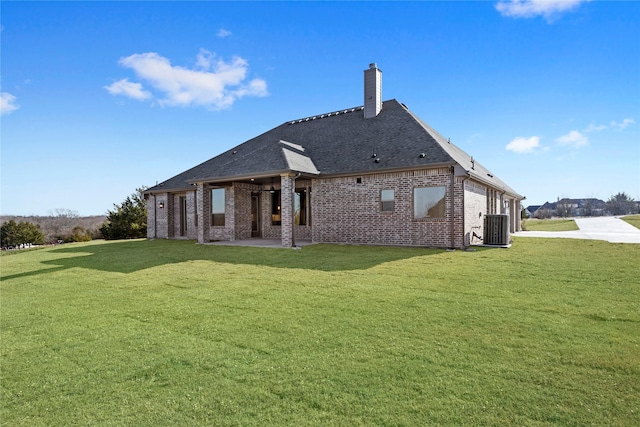 back of house with a chimney, a lawn, central AC, and brick siding