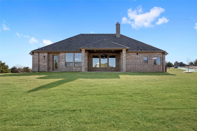 rear view of property featuring brick siding, a yard, a chimney, and roof with shingles