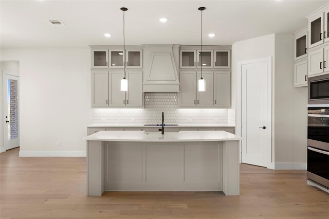 kitchen featuring hanging light fixtures, a center island with sink, light wood-type flooring, custom range hood, and stainless steel appliances