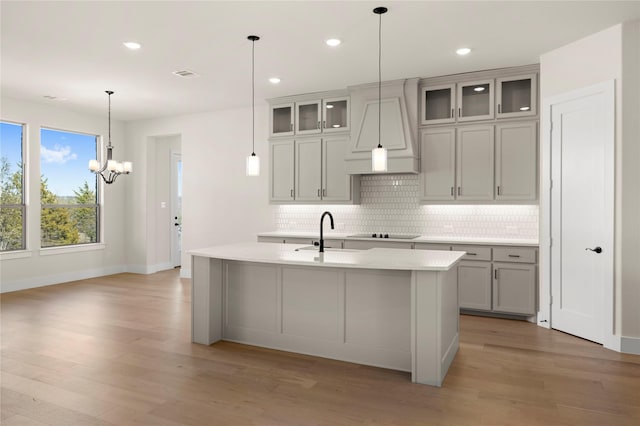 kitchen featuring glass insert cabinets, black electric cooktop, light countertops, gray cabinetry, and a sink