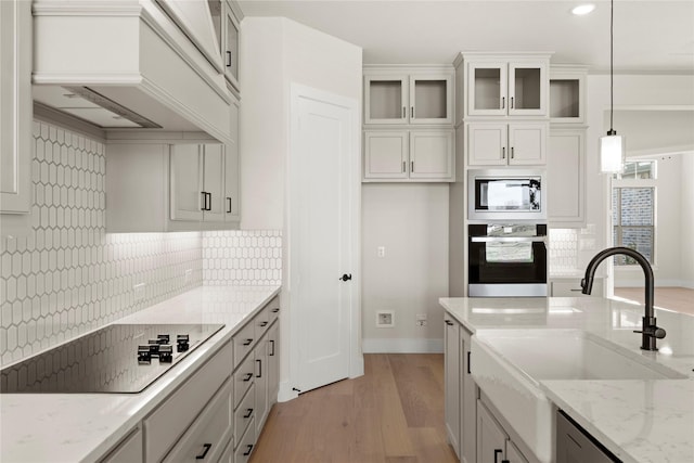 kitchen with black appliances, light stone countertops, glass insert cabinets, and pendant lighting