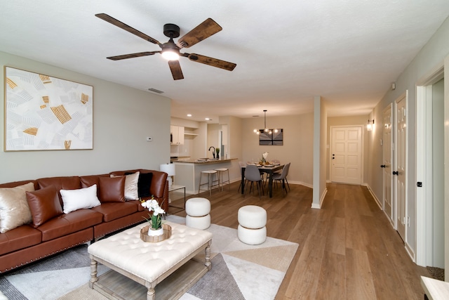 living room featuring sink, ceiling fan with notable chandelier, and light hardwood / wood-style floors