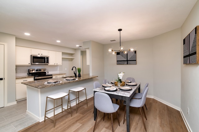 dining area with an inviting chandelier, light wood-type flooring, and sink