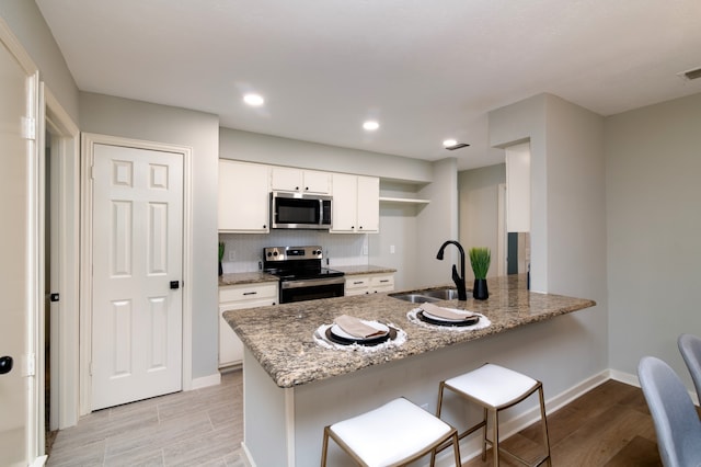 kitchen with light stone counters, sink, kitchen peninsula, white cabinetry, and stainless steel appliances