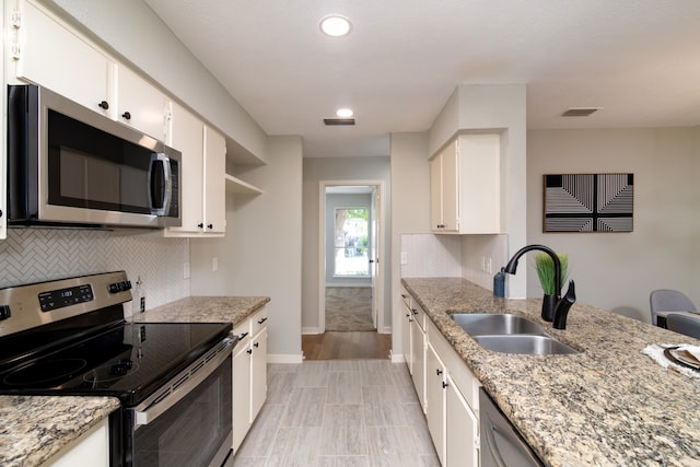 kitchen with light stone counters, appliances with stainless steel finishes, sink, and white cabinetry