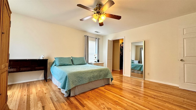 bedroom with a spacious closet, a closet, ceiling fan, and light hardwood / wood-style flooring