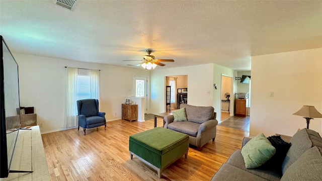 living room with a textured ceiling, light hardwood / wood-style floors, and ceiling fan