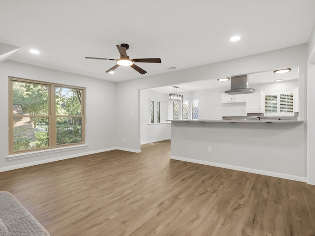 unfurnished living room with ceiling fan with notable chandelier and light hardwood / wood-style floors