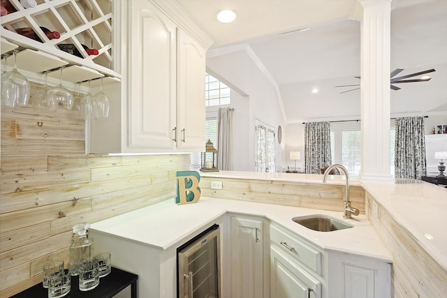 kitchen with ceiling fan, white cabinets, sink, beverage cooler, and decorative columns