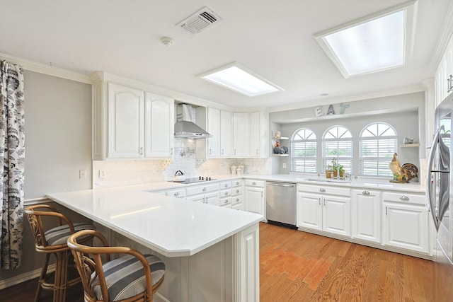 kitchen with light hardwood / wood-style flooring, kitchen peninsula, appliances with stainless steel finishes, and wall chimney range hood