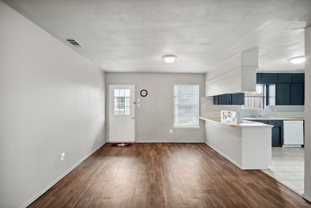 kitchen featuring dishwasher, dark hardwood / wood-style floors, kitchen peninsula, blue cabinetry, and tasteful backsplash