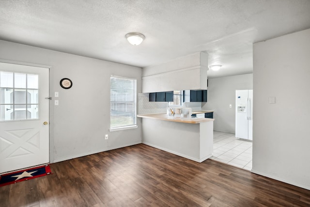 kitchen featuring kitchen peninsula, hardwood / wood-style floors, tasteful backsplash, white cabinetry, and white refrigerator with ice dispenser