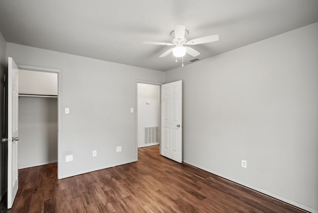 unfurnished bedroom featuring a walk in closet, dark hardwood / wood-style floors, a closet, and ceiling fan