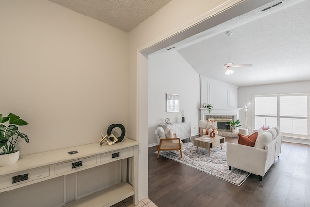 living room featuring vaulted ceiling, a fireplace, ceiling fan, dark wood-type flooring, and a textured ceiling