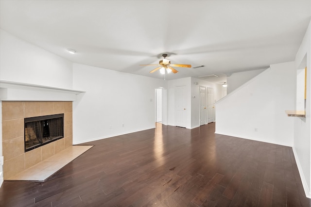 unfurnished living room featuring dark hardwood / wood-style floors, a tiled fireplace, and ceiling fan