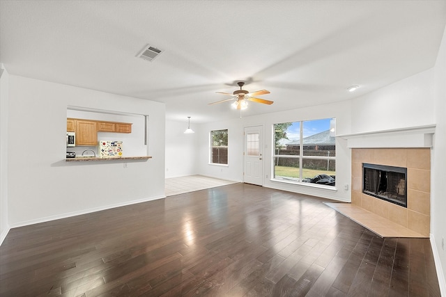 unfurnished living room with ceiling fan, a fireplace, and dark wood-type flooring