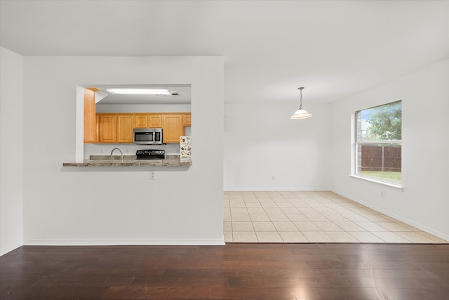 kitchen with pendant lighting, light brown cabinets, kitchen peninsula, black range, and light hardwood / wood-style flooring