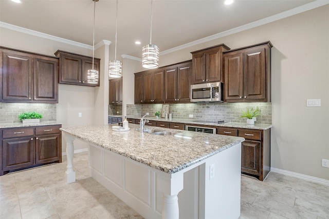 kitchen featuring appliances with stainless steel finishes, light stone counters, an island with sink, decorative light fixtures, and sink