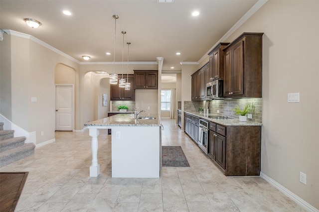 kitchen with light stone countertops, pendant lighting, stainless steel appliances, a center island with sink, and ornamental molding