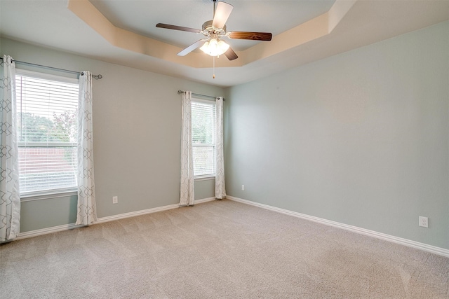 empty room featuring a raised ceiling, light carpet, ceiling fan, and a wealth of natural light