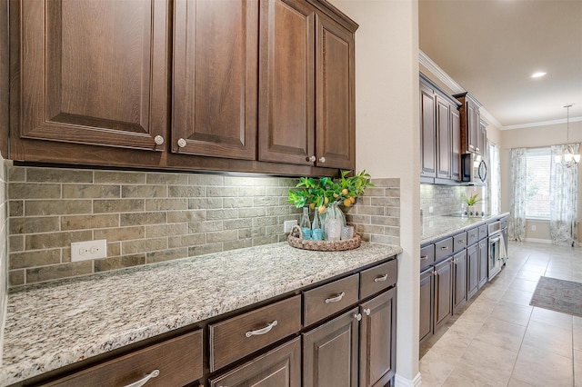 kitchen featuring light stone counters, tasteful backsplash, hanging light fixtures, dark brown cabinetry, and crown molding