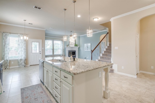 kitchen with a kitchen island with sink, light stone countertops, pendant lighting, stainless steel dishwasher, and ornamental molding