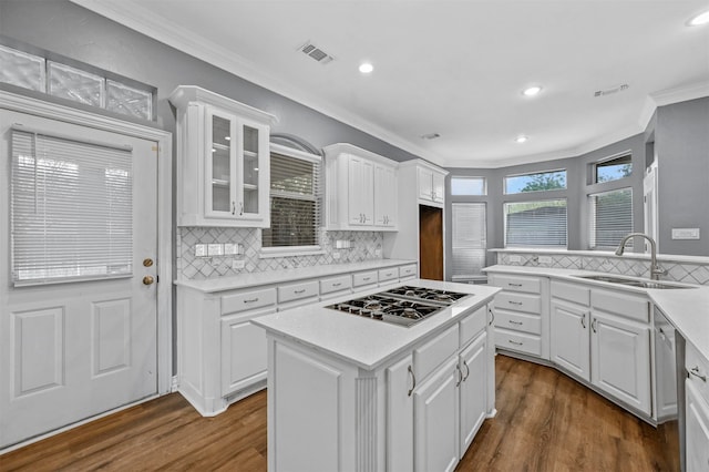 kitchen featuring white cabinets, dark wood-type flooring, stainless steel gas stovetop, a center island, and crown molding