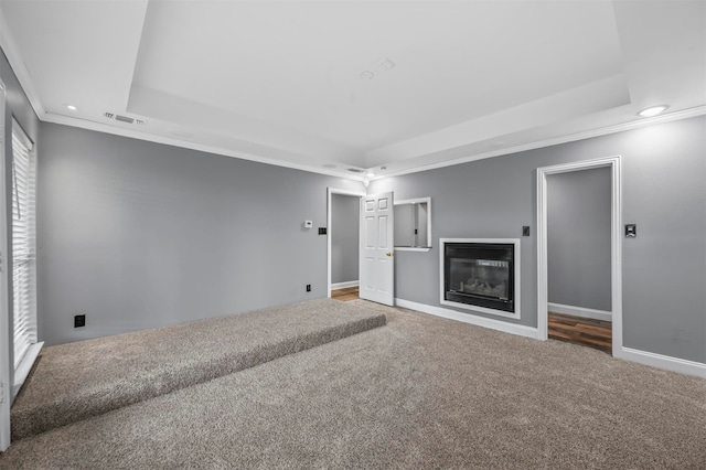 unfurnished living room featuring carpet floors, a raised ceiling, and ornamental molding