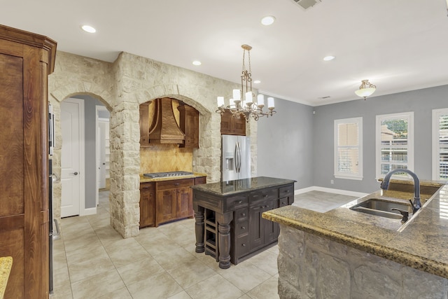 kitchen with sink, a kitchen island, custom range hood, appliances with stainless steel finishes, and decorative light fixtures