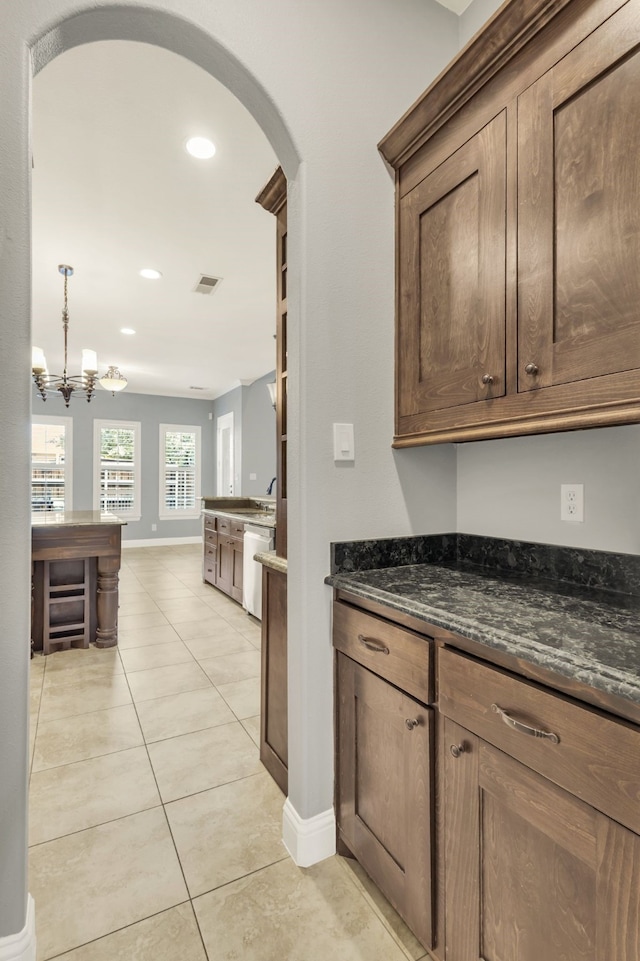 kitchen with light tile patterned flooring, dishwasher, decorative light fixtures, dark stone counters, and a notable chandelier