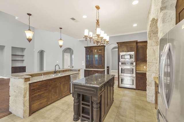 kitchen with appliances with stainless steel finishes, light stone countertops, decorative light fixtures, a large island, and a notable chandelier