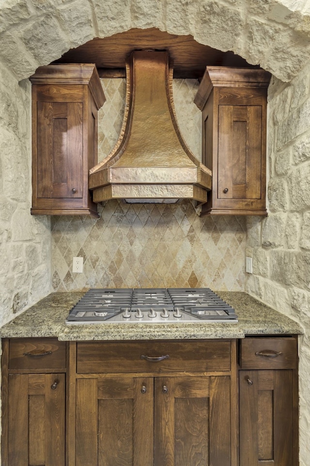 kitchen with stainless steel gas stovetop, dark stone countertops, backsplash, and premium range hood