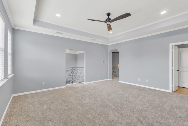 spare room with a raised ceiling, crown molding, ceiling fan, and light colored carpet