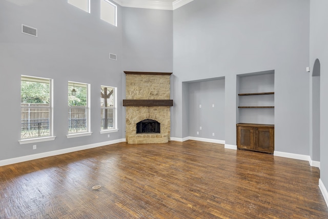 unfurnished living room featuring a stone fireplace, a high ceiling, dark hardwood / wood-style floors, and built in features