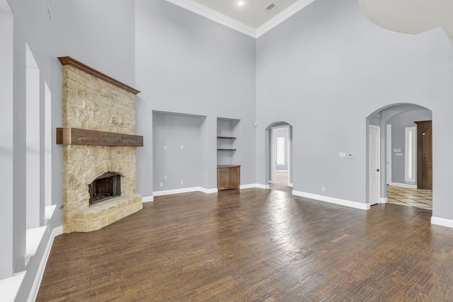 unfurnished living room featuring a stone fireplace, ornamental molding, a towering ceiling, and dark hardwood / wood-style floors